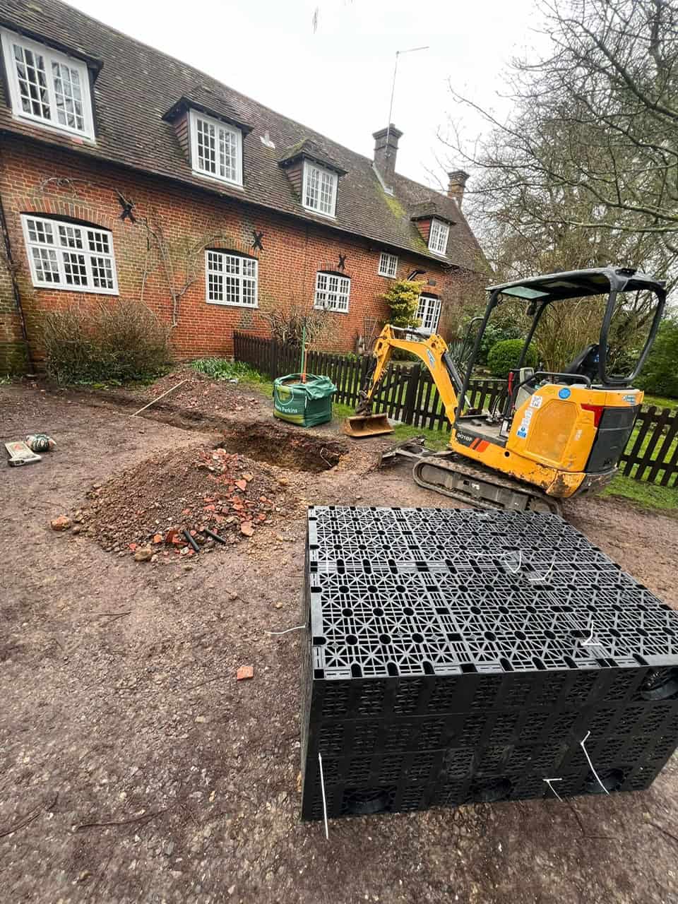 Excavator installing drainage system in a residential garden.